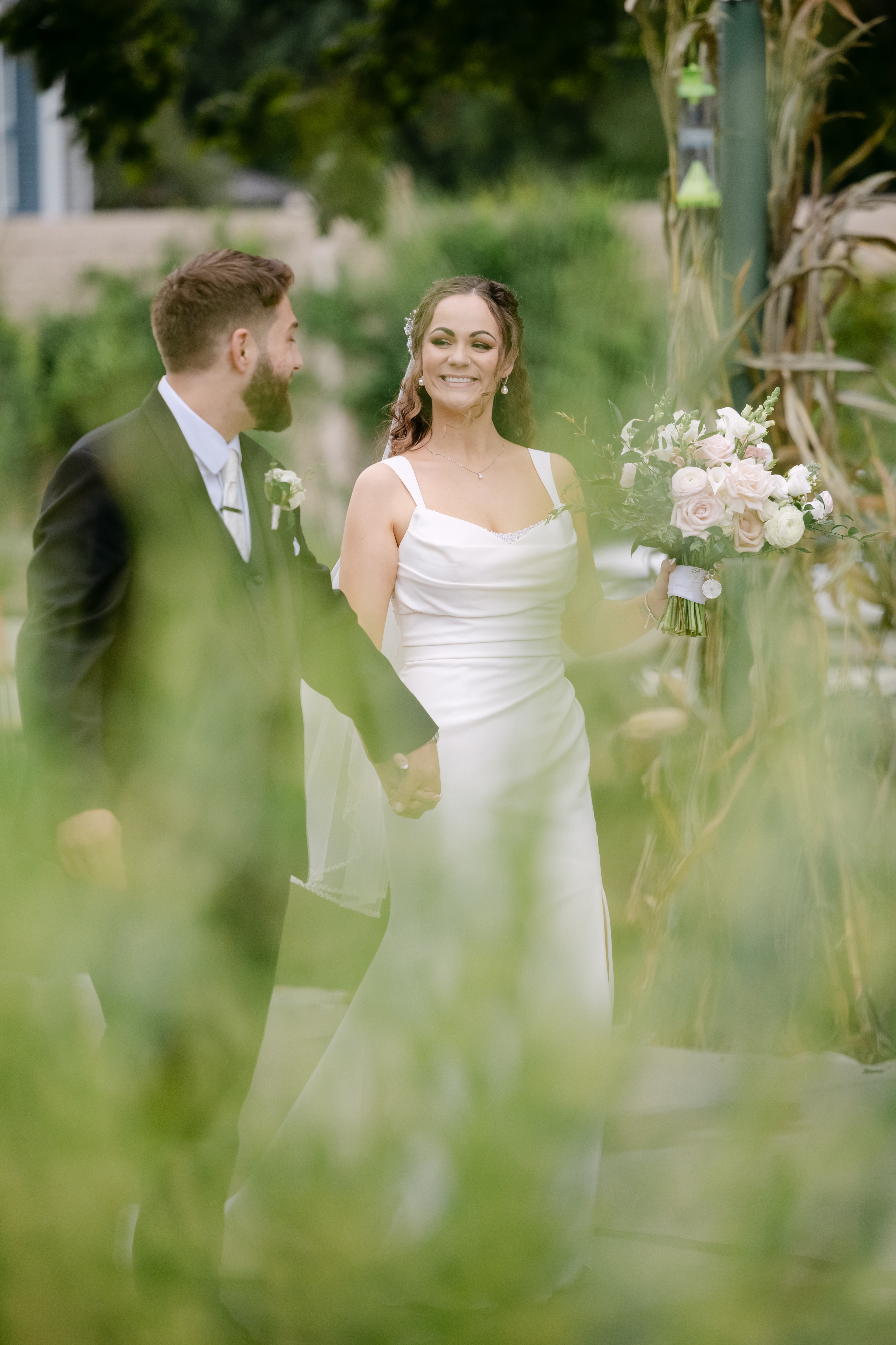 A bride and groom walking hand in hand through tall grass